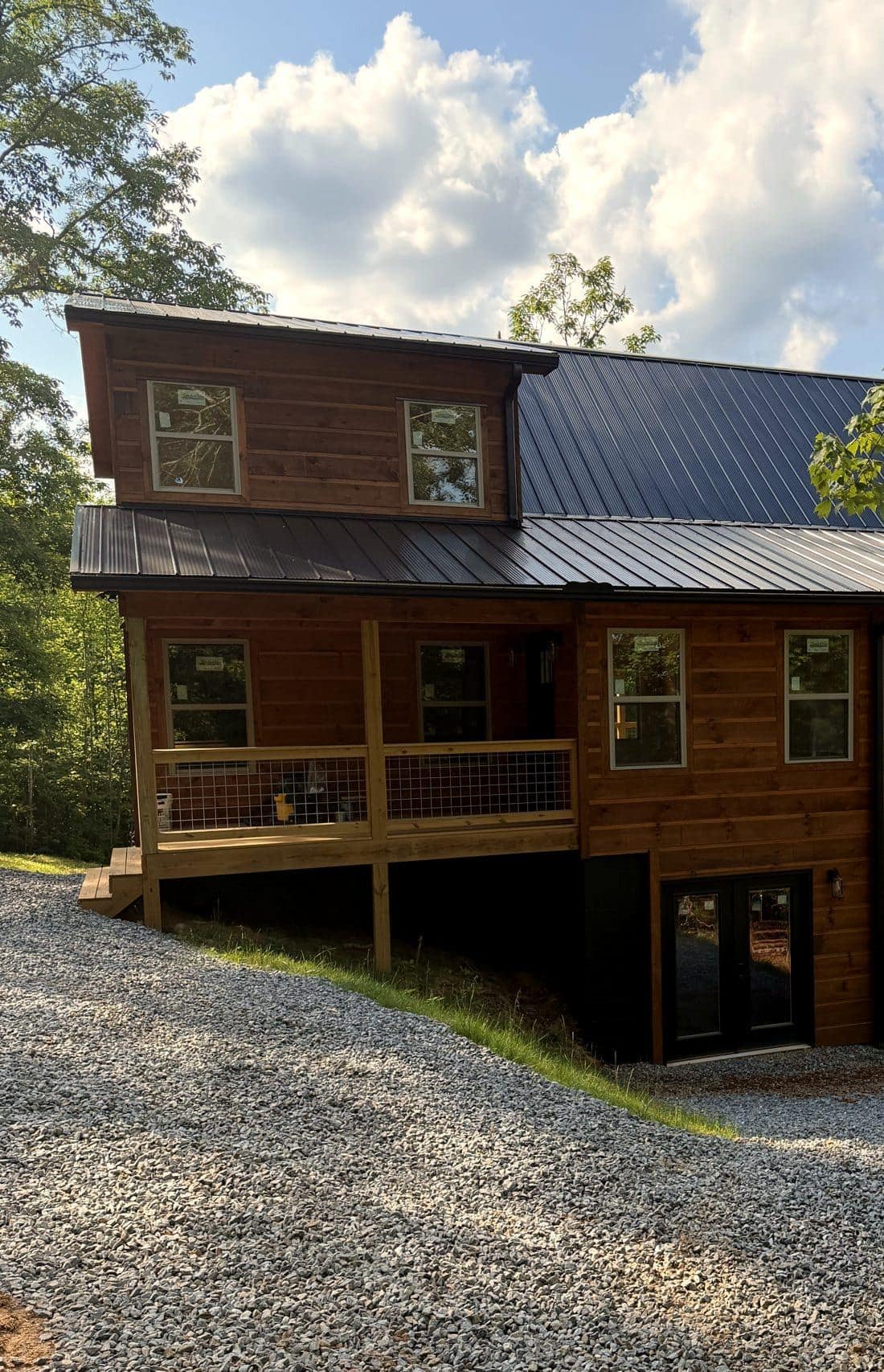 Wood-sided home with a metal roof, a covered porch, and a gravel drive