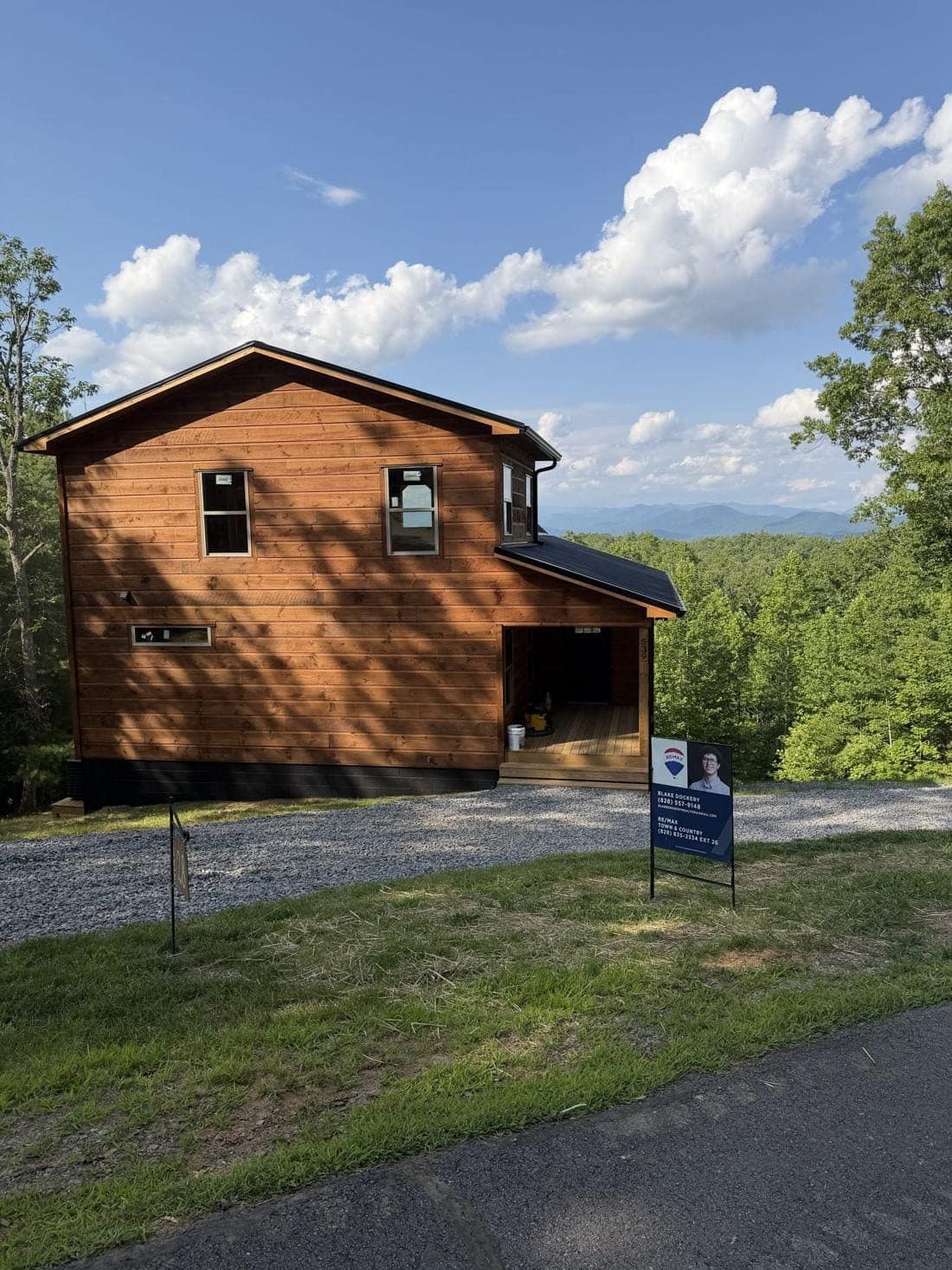 Two-story wood-sided home with a gravel drive and mountains behind it