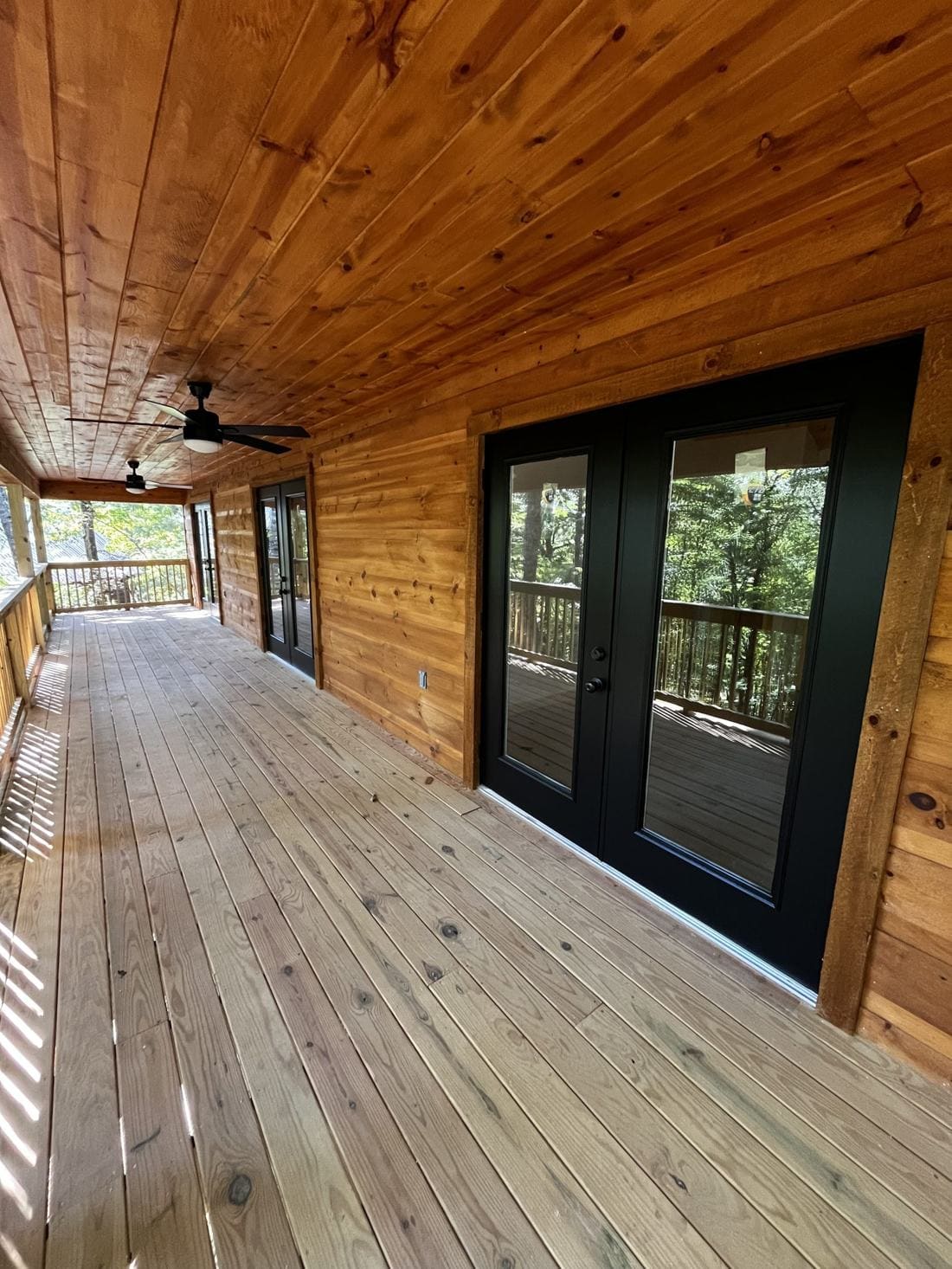 Long covered porch with wood ceiling and black French doors