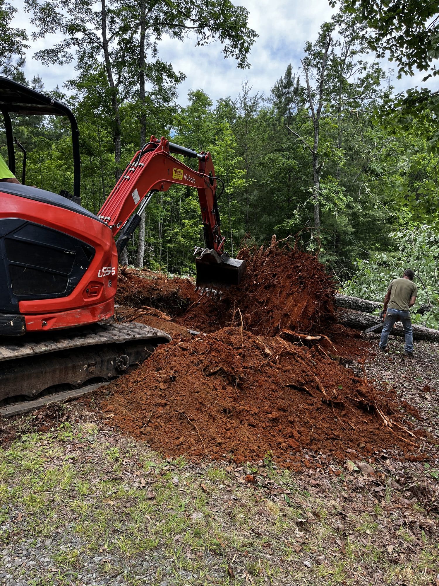 Red mini excavator digging red clay on a wooded lot