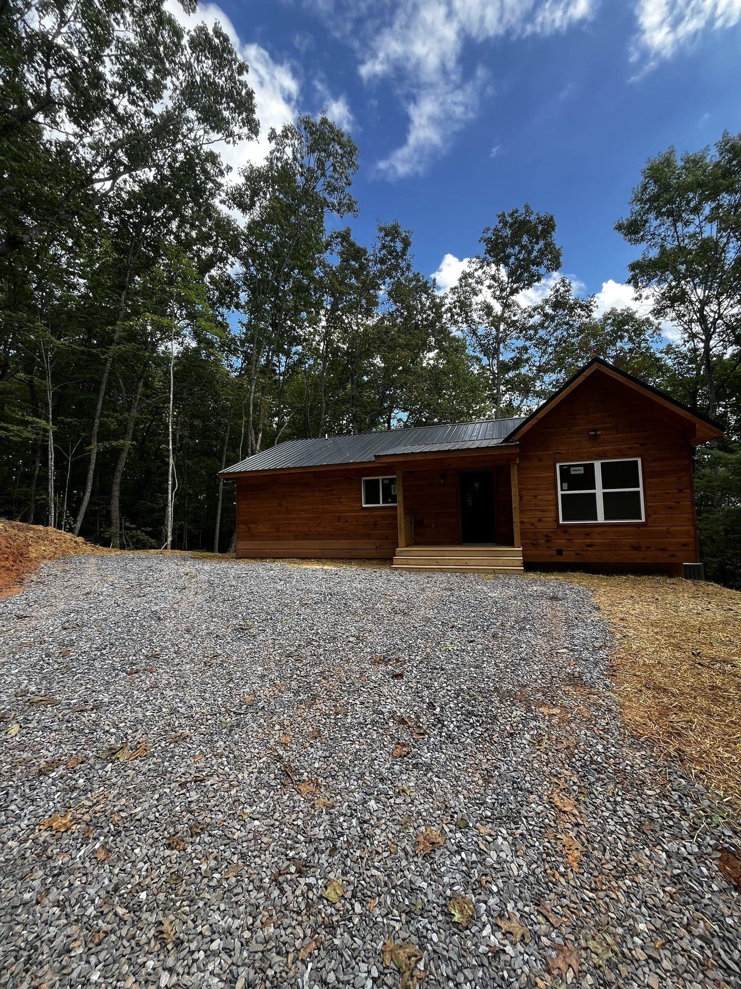 Stained wood cabin at the end of a wide gravel driveway