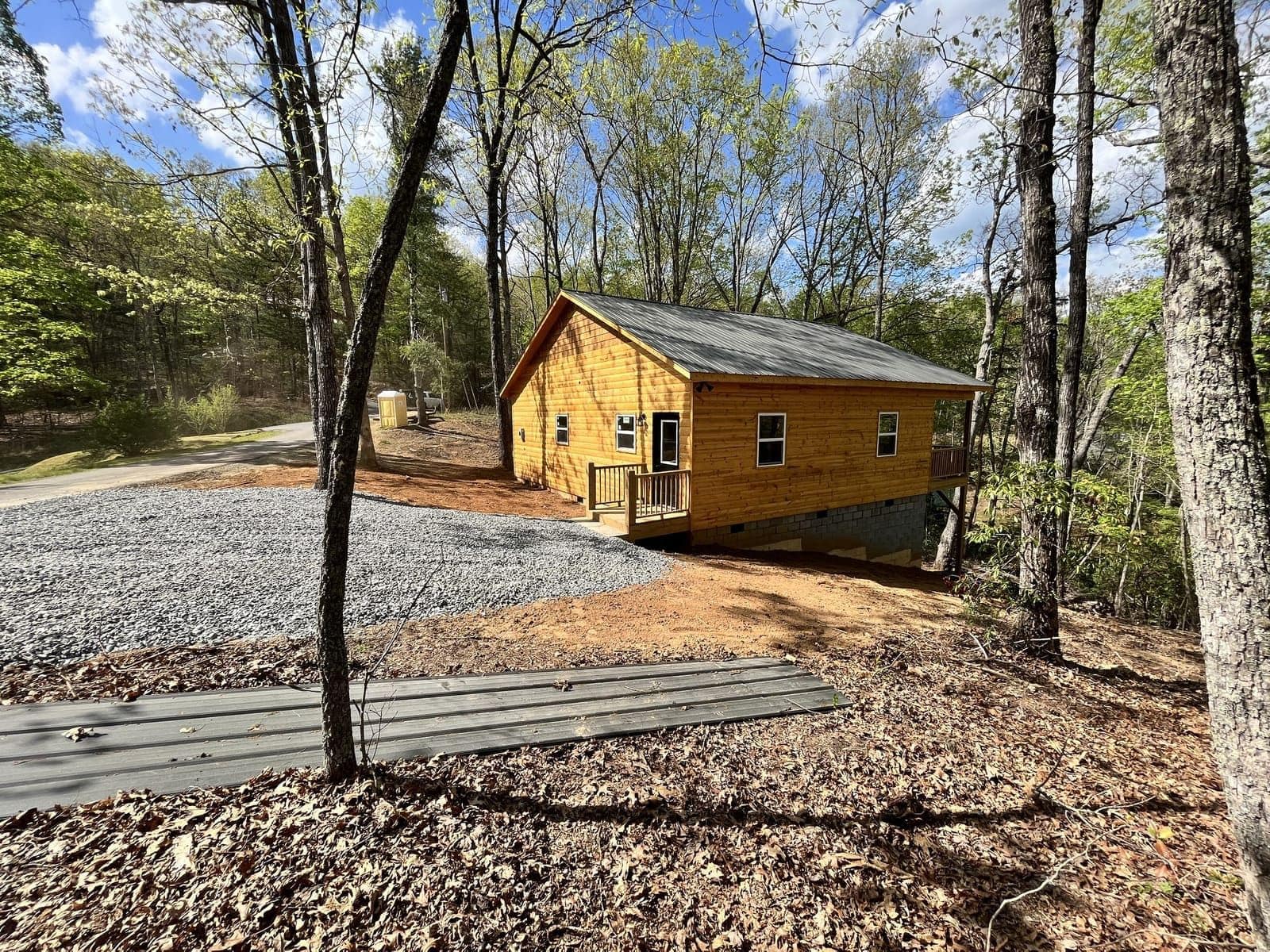 Side view of wood-sided cabin with gravel pad and wooded hillside