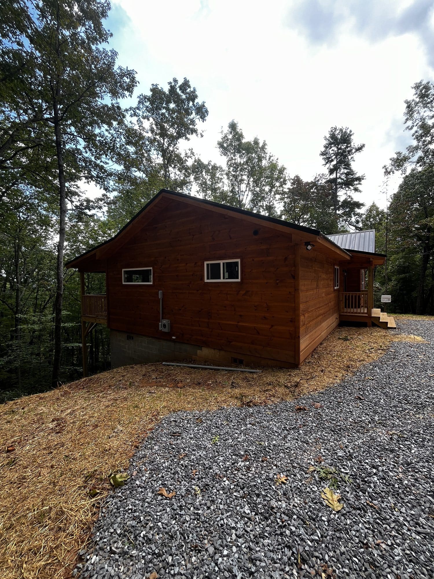 Side of a stained wood cabin with gravel drive and trees