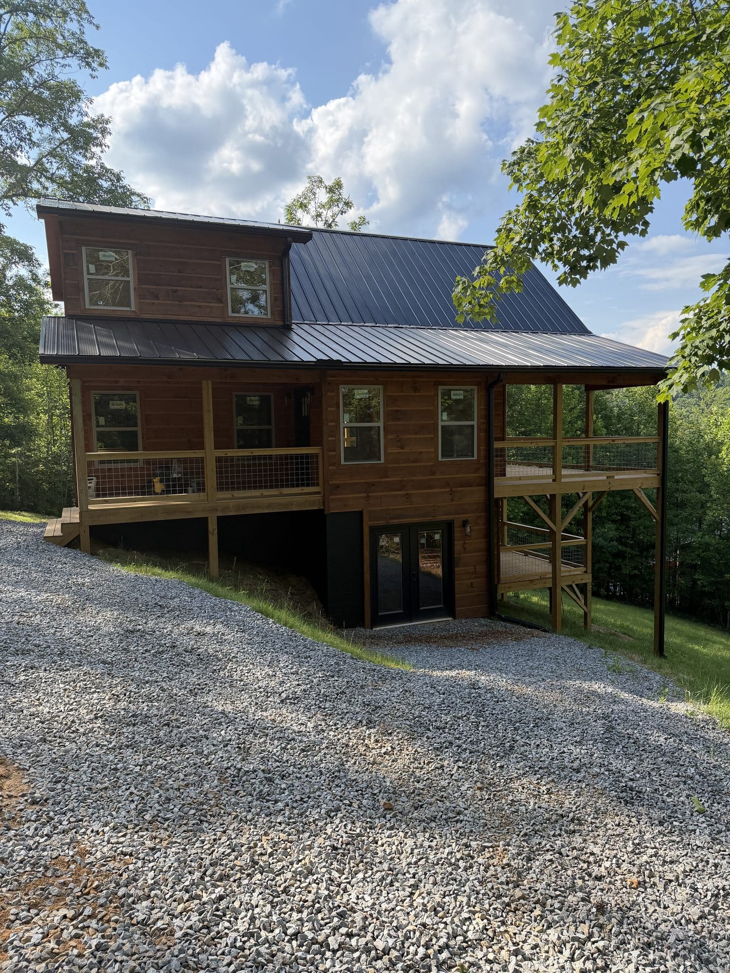 Two-story cabin with covered raised porch on posts above gravel