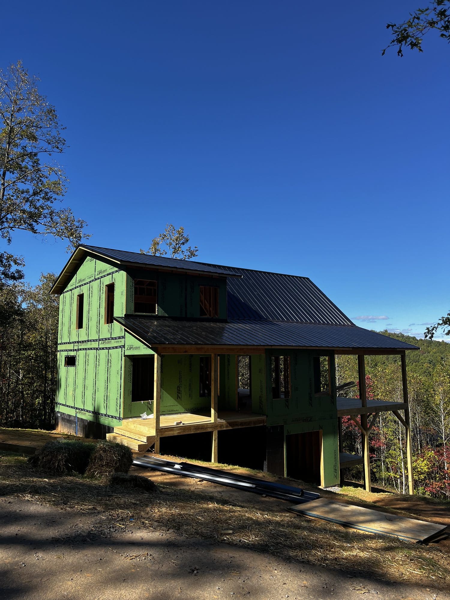 Green-sided two-story home with dark metal roof and porch