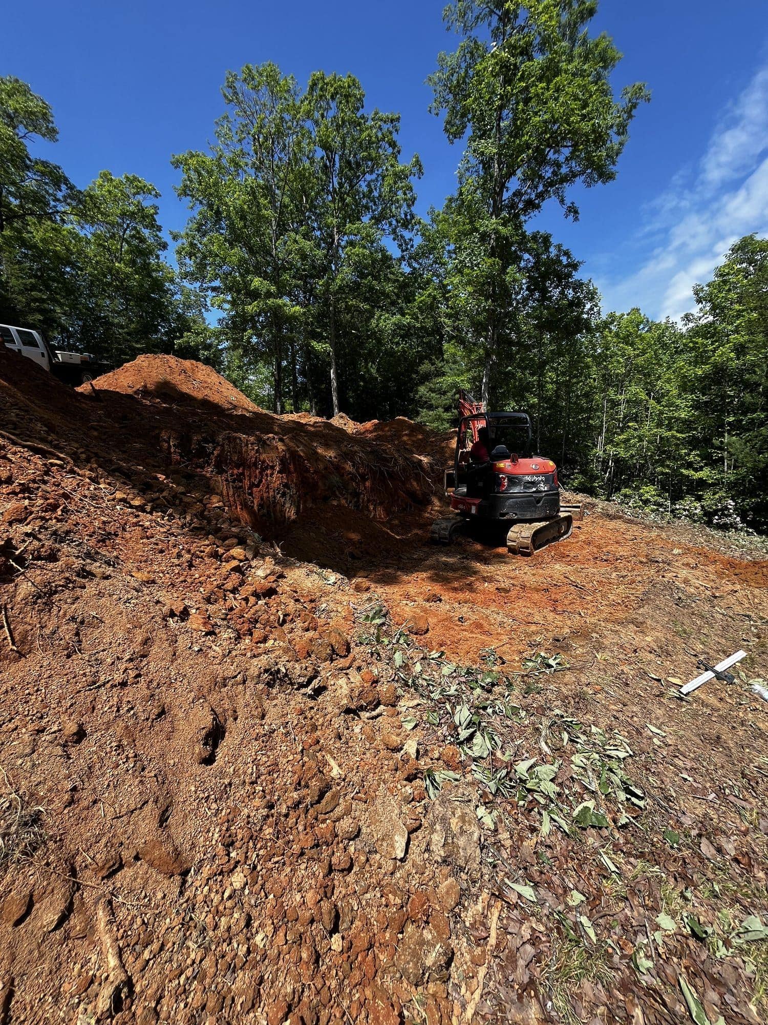 Freshly cut red clay slope with excavator in trees