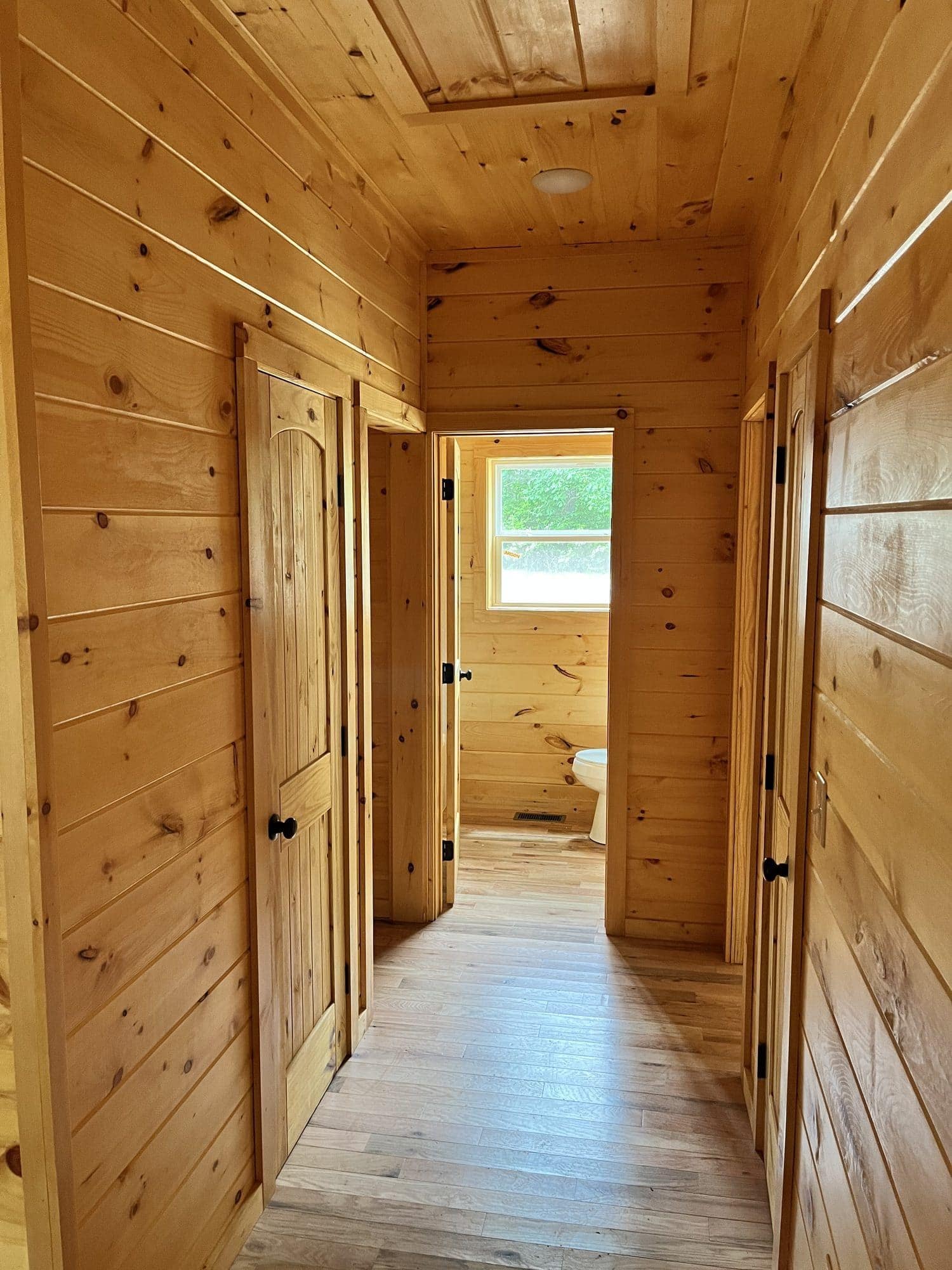 Pine-paneled hallway with light wood flooring and doors along both sides