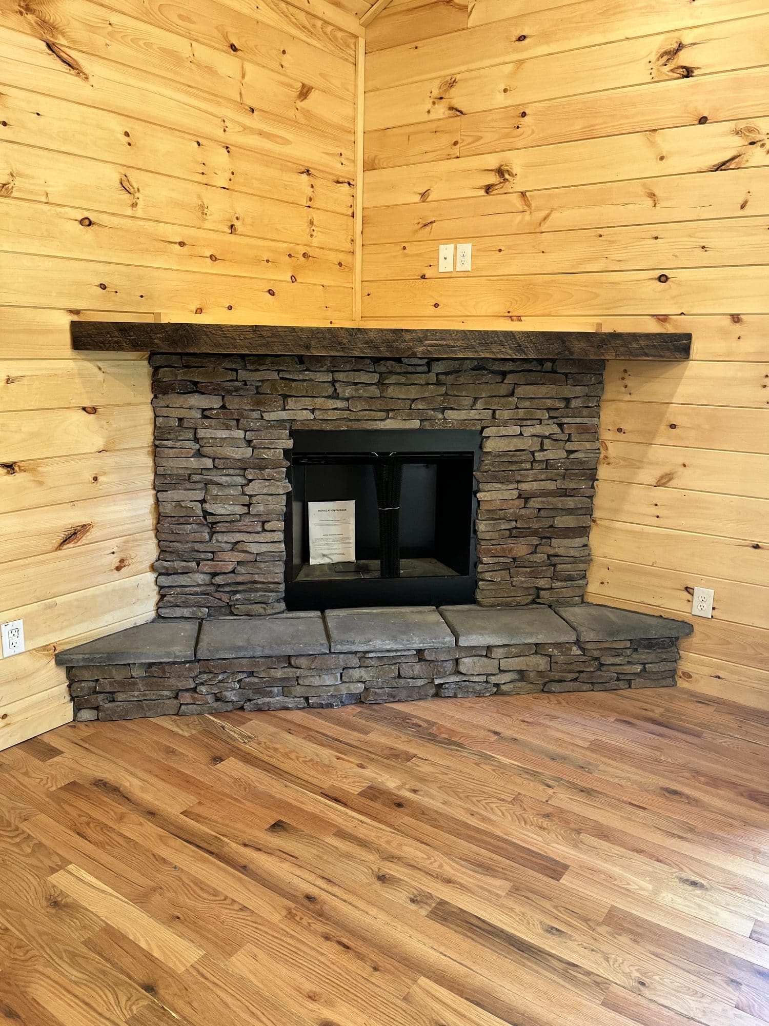 Stacked-stone corner fireplace in a pine-paneled room