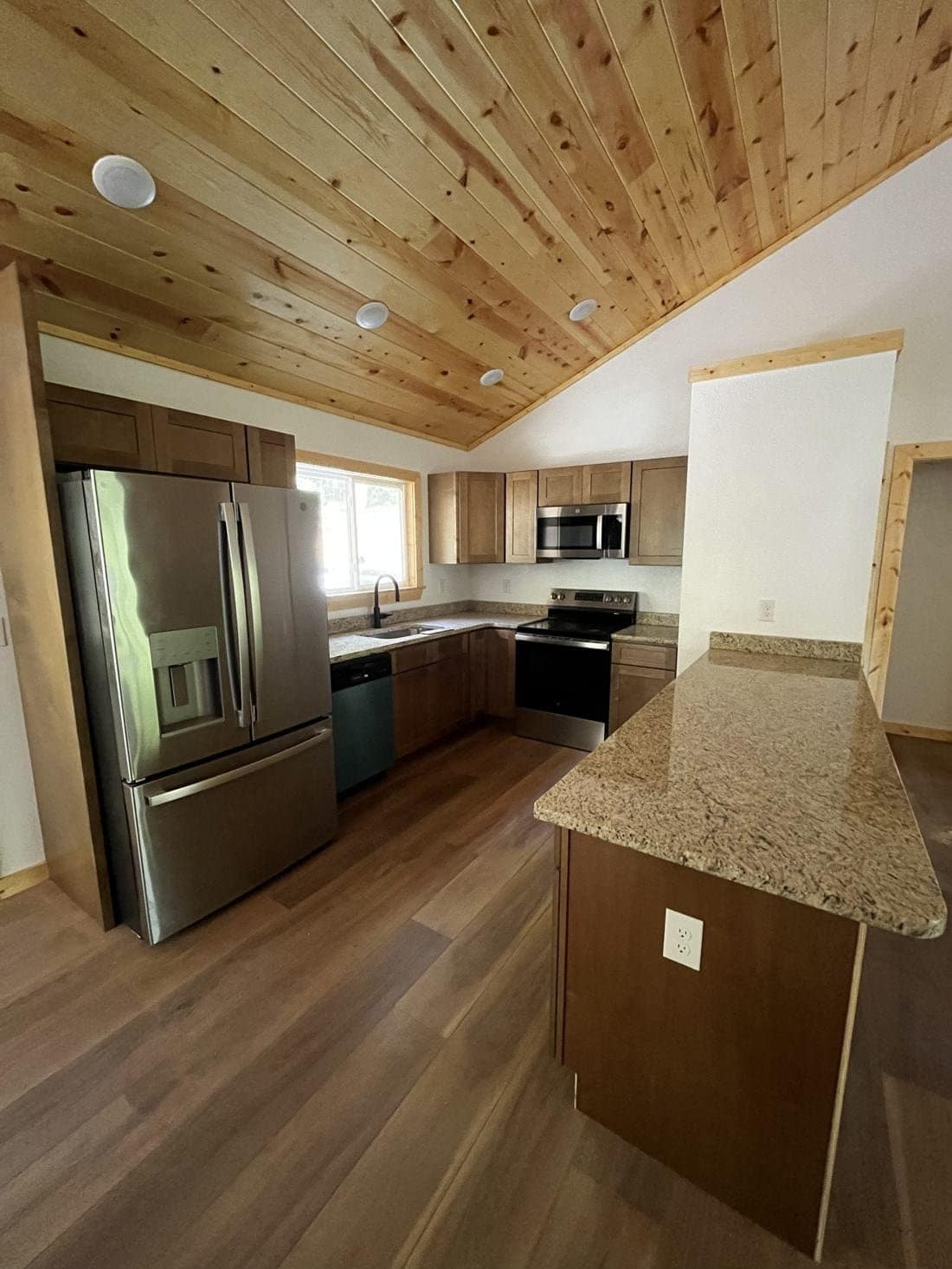 Kitchen with island and stainless appliances under a wood ceiling