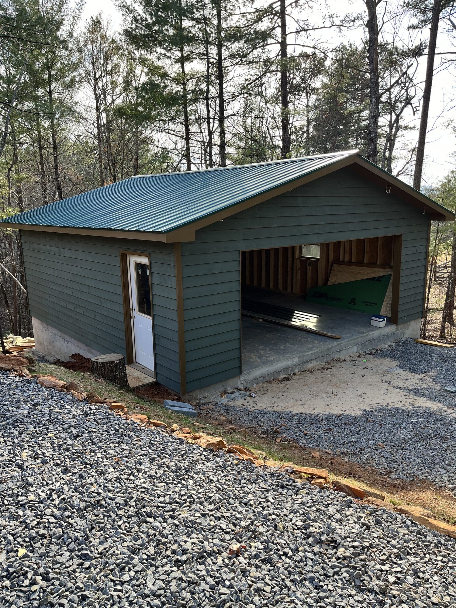 Green-sided garage with gravel apron in the woods