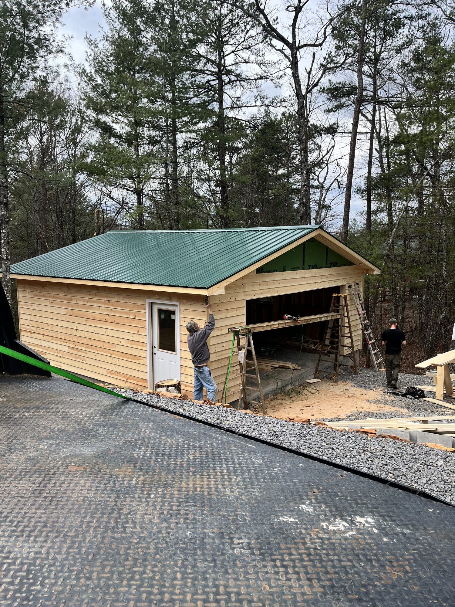Wood-sided garage with green metal roof on gravel pad