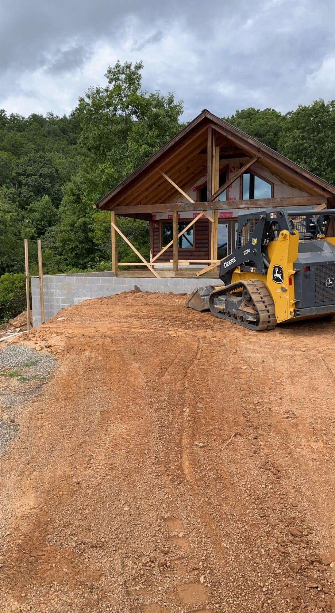 Skid steer working dirt beside a timber-frame structure